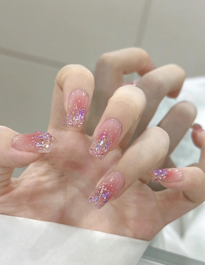 mau-nail-nhu-dep__52__152ba59d40d84e14813659c5f476908a Bàn tay với móng tay dài được sơn màu hồng nhạt, trang trí lấp lánh và hoa văn ánh kim.