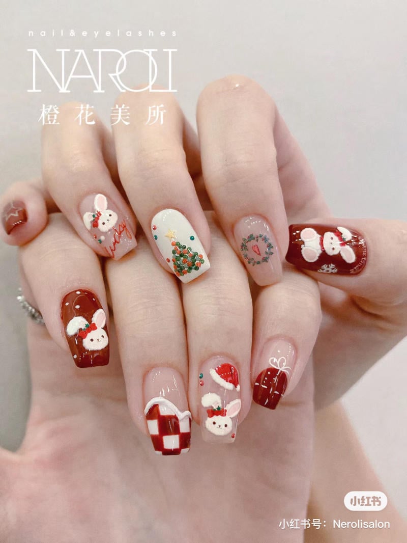 mau-nail-noel-dep__18__8da66b8731be4884bc1c82861c4dd4bf Bàn tay với móng tay được trang trí họa tiết mùa đông và hình thỏ, phối màu đỏ, trắng, và xanh lá cây.