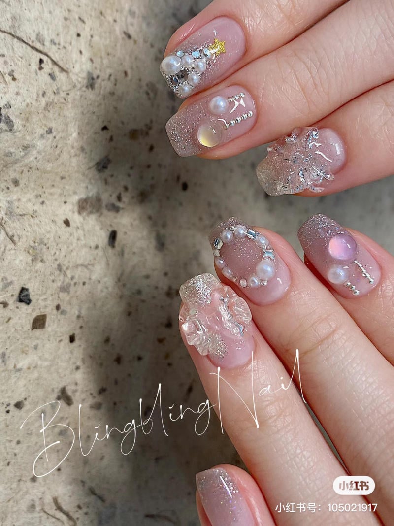 mau-nail-noel-dep__19__d84c4e4759504bdf8616ea4235199220 Bàn tay với móng tay trang trí cầu kỳ, đính đá và ngọc trai, nền đá granit.