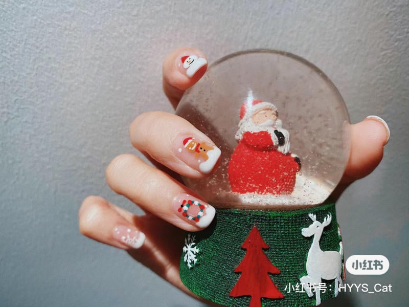 mau-nail-noel-dep__20__08b15638a7874567ad47c67478e87bf8 Bàn tay với móng tay trang trí Giáng Sinh cầm quả cầu tuyết có hình ông già Noel và đế trang trí tuần lộc.