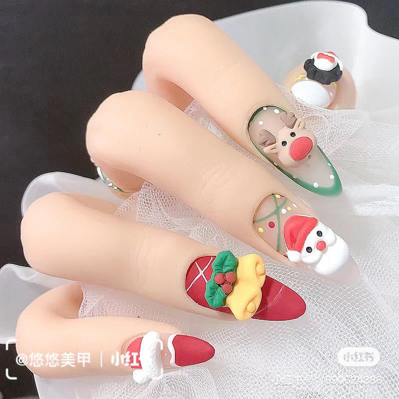 mau-nail-noel-dep__27__cb576d983a054939bacec1e97a01cb02 Bàn tay với móng tay trang trí họa tiết Giáng Sinh, gồm tuần lộc, ông già Noel và chuông.