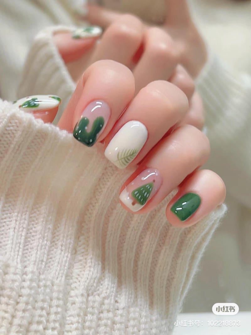 mau-nail-noel-dep__30__b28a156a89744ec4baf96b41ecb95b67 Móng tay với họa tiết cây xanh trên nền trắng, được giữ trong tay áo len màu trắng.