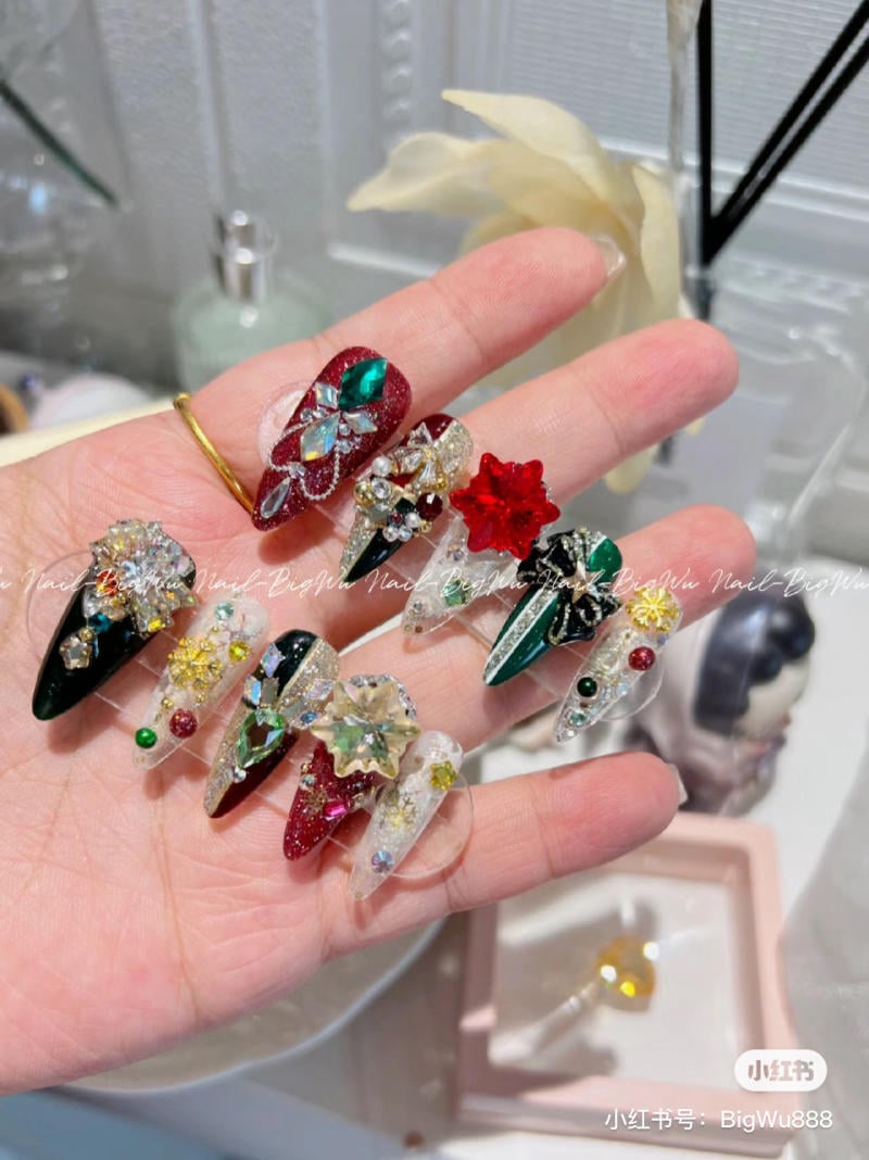 mau-nail-noel-dep__34__95fa27a6c52b47ba89717e45d84e43aa Bộ móng tay giả với hoa văn và đá quý nhiều màu sắc được trưng bày trên bàn tay.