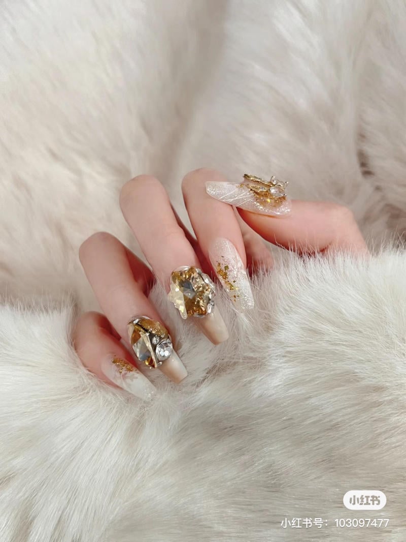 mau-nail-noel-dep__41__8c491c5345244bbe9c417ebcc2582c45 Bàn tay với móng tay được trang trí bằng đá quý và ánh kim, đặt trên nền lông mềm mại.