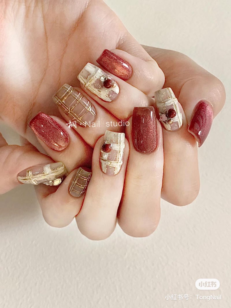 mau-nail-noel-dep__45__6fab5cc046e74fef954415c739ff8f6e Bàn tay với móng tay được trang trí họa tiết màu đỏ và vàng, kết hợp các hoa văn và đính đá nhỏ.