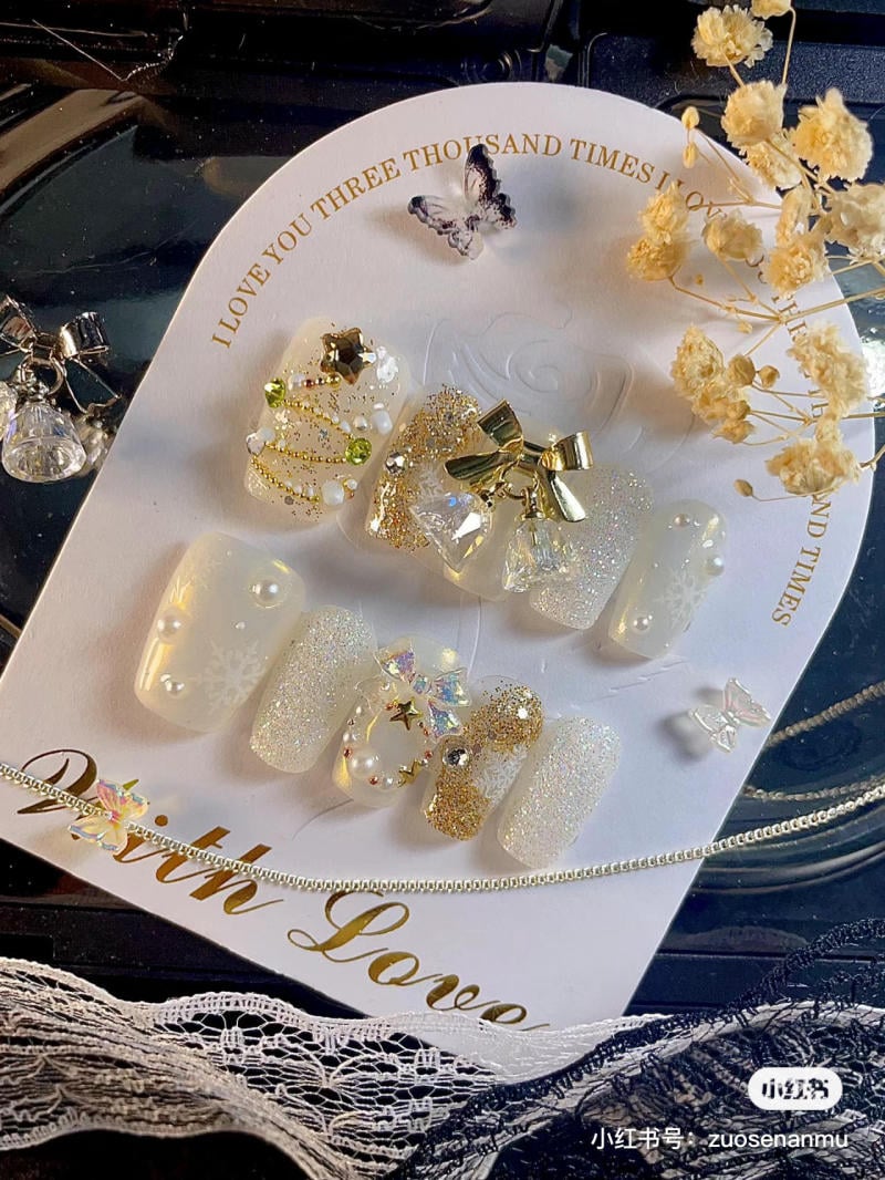 mau-nail-noel-dep__61__52327aa45a6143fc9f37d5211a7832ad Bộ móng giả trang trí họa tiết lấp lánh và phụ kiện trên nền thẻ trắng, kèm hoa khô và dây chuyền nhỏ.