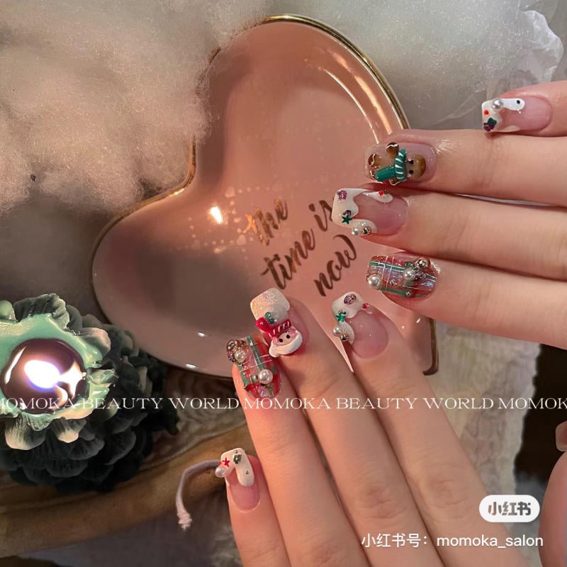 mau-nail-noel-dep__6__d250a52487d645628efdf789c48ad0d5 Bàn tay với móng tay được trang trí họa tiết lễ hội, bên cạnh là đĩa hình trái tim và nến đang cháy.