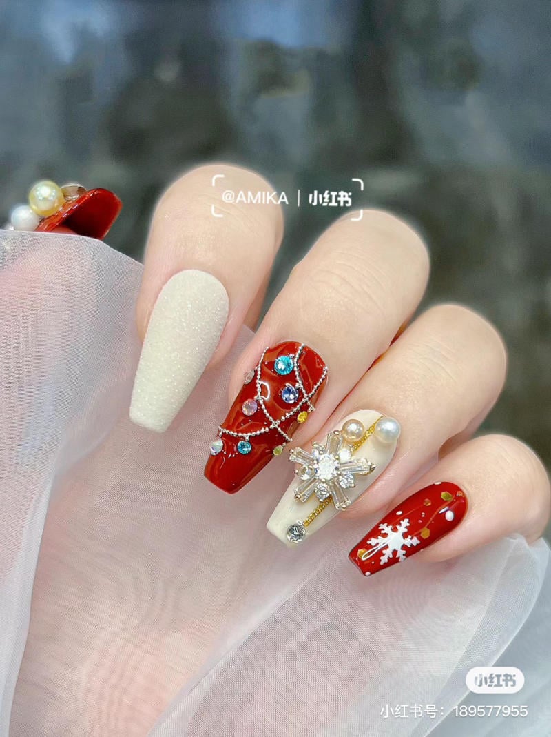 B&agrave;n tay với m&oacute;ng tay được trang tr&iacute; cầu kỳ, m&agrave;u đỏ v&agrave; trắng, đ&iacute;nh đ&aacute;, hoa tuyết v&agrave; ngọc trai.