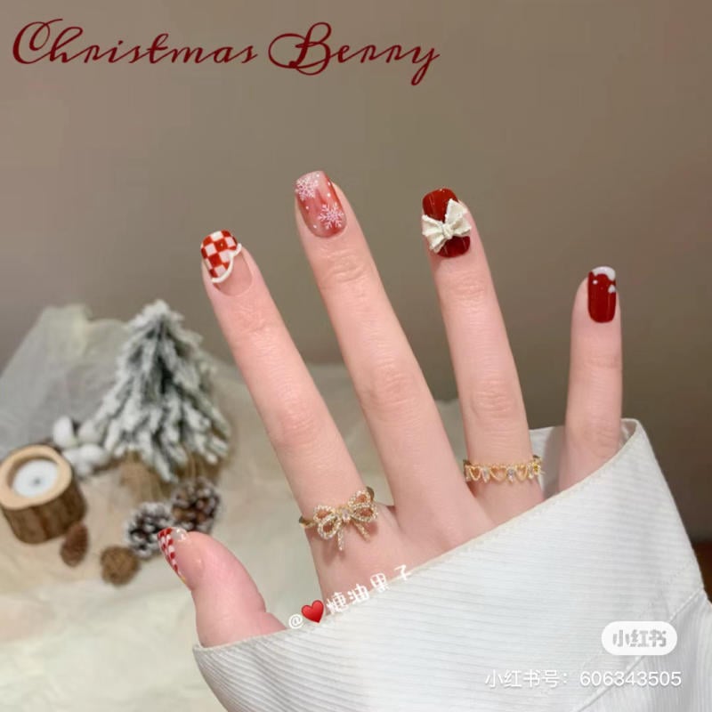 mau-nail-noel-dep__84__374a88c9380640dab9cce243dec96bcf Bàn tay với móng tay được sơn màu đỏ và họa tiết lễ hội, nền là cây thông phủ tuyết và nến trang trí.