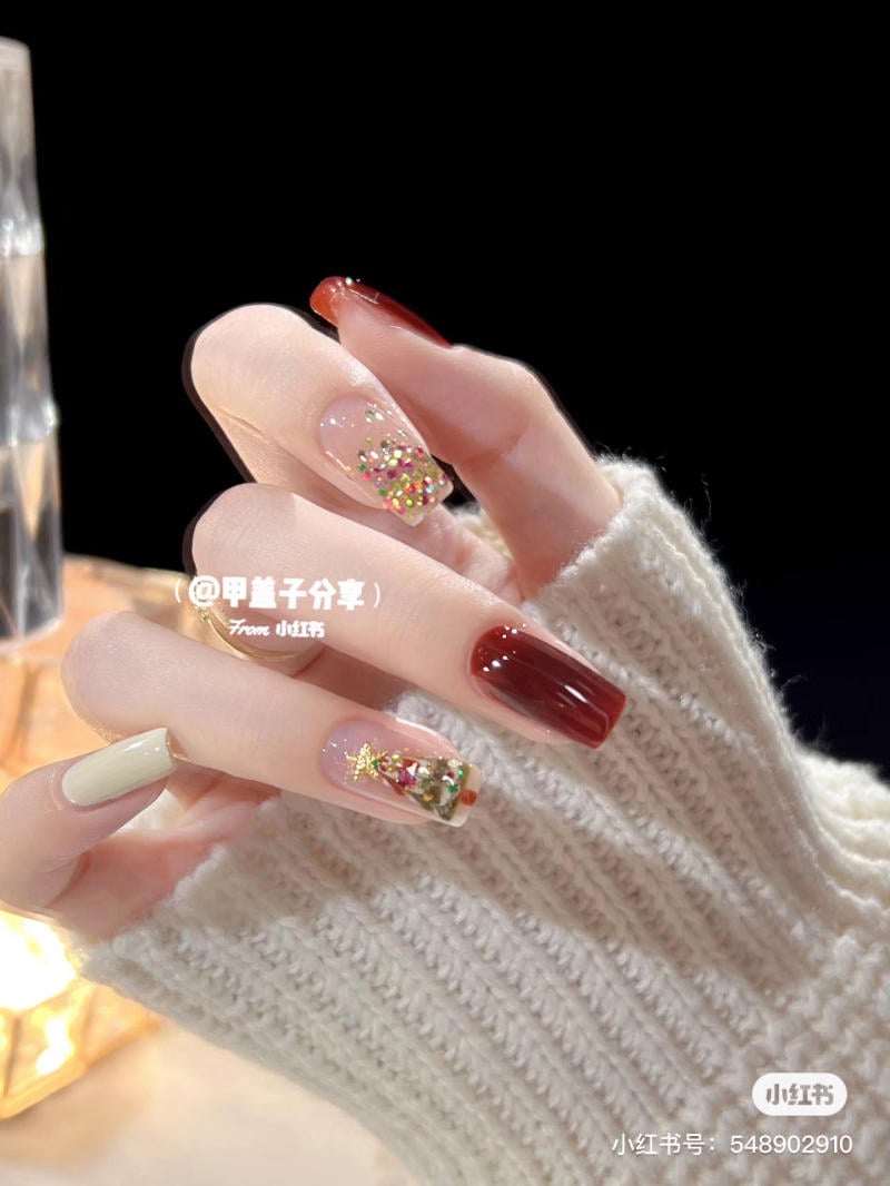 mau-nail-noel-dep__8__ac4c7df96b054e1ea78f6e39e9c8125b Bàn tay với móng tay sơn màu đỏ, trắng và trang trí kim tuyến, trên nền tối.