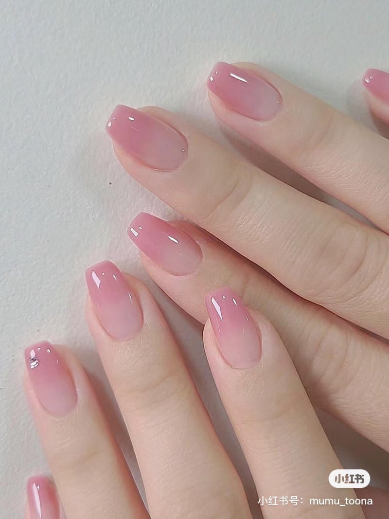Bàn tay với móng tay sơn màu hồng nhạt, bóng loáng, trên nền trắng.