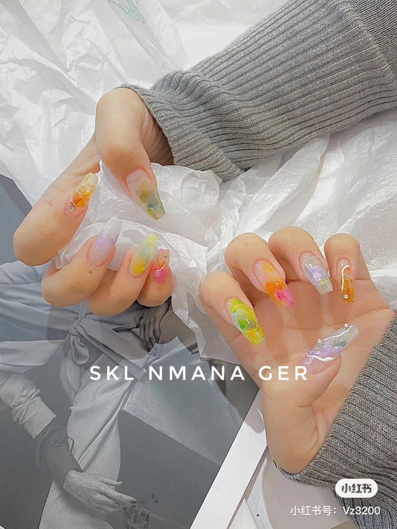 Tay đeo móng giả, sơn màu sắc sặc sỡ, trên nền giấy màu trắng, áo len xám.