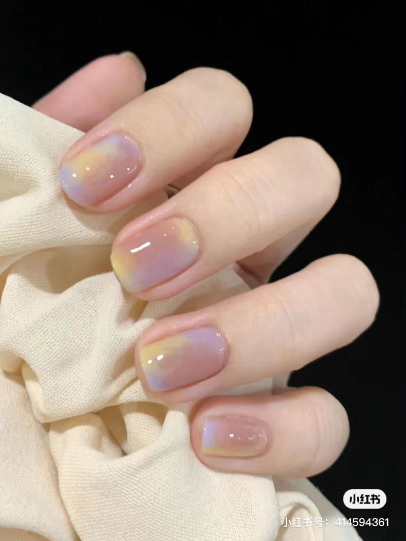 Bàn tay với móng tay được sơn màu pastel, cầm một mảnh vải màu kem, nền tối.