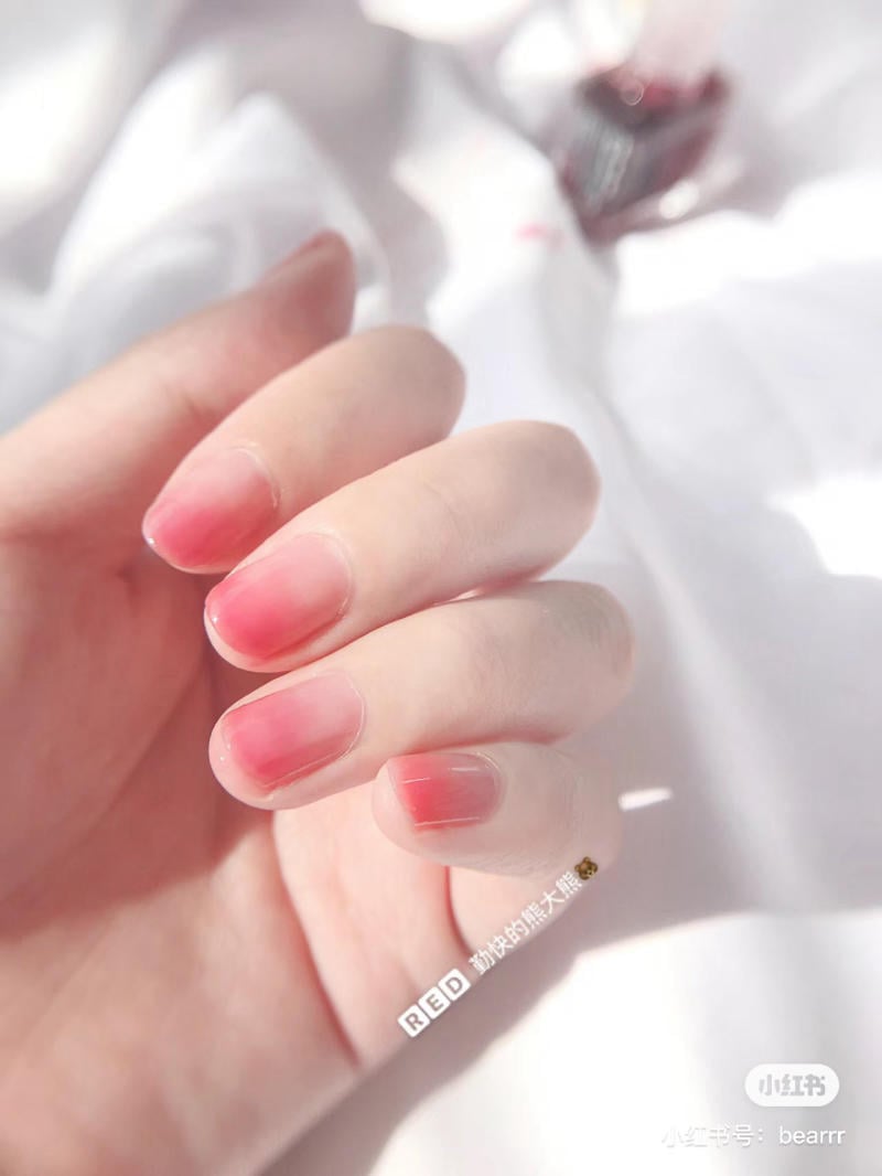 Bàn tay với móng tay được sơn màu hồng nhạt trên nền vải trắng mềm mại.
