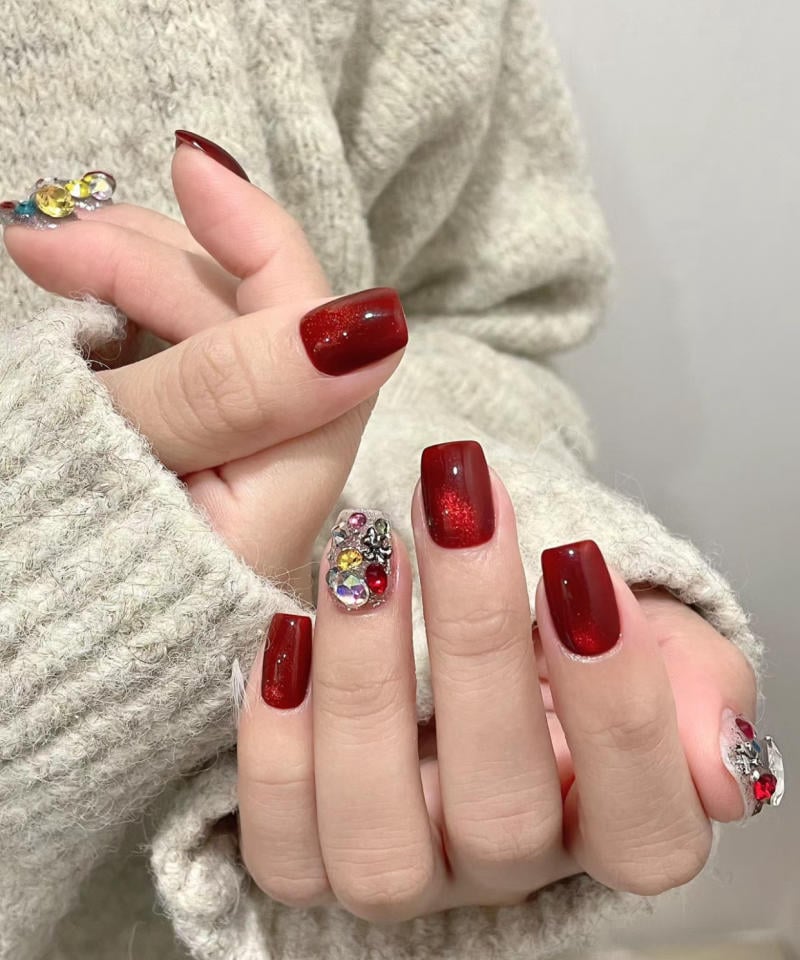 Bàn tay với móng tay sơn màu đỏ và trang trí đá lấp lánh, mặc áo len màu xám nhạt.
