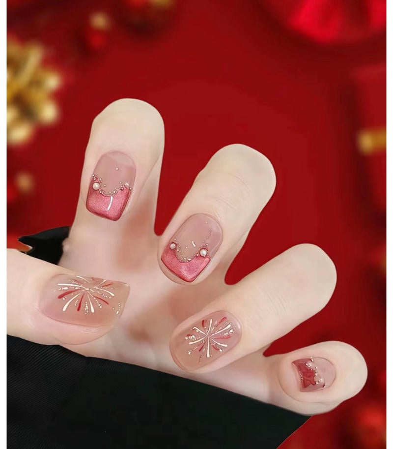 Bàn tay với móng tay được trang trí họa tiết đỏ và kim tuyến, nền màu đỏ, tạo cảm giác lễ hội và sang trọng.