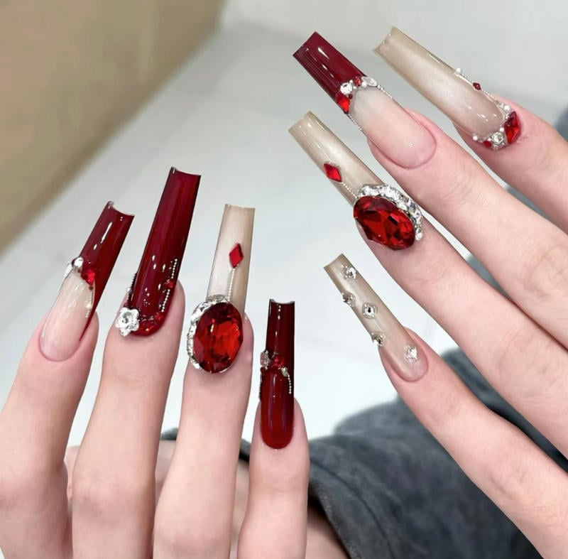 Bàn tay với móng tay dài được trang trí bằng màu đỏ và đính đá, tạo phong cách nổi bật và sang trọng.