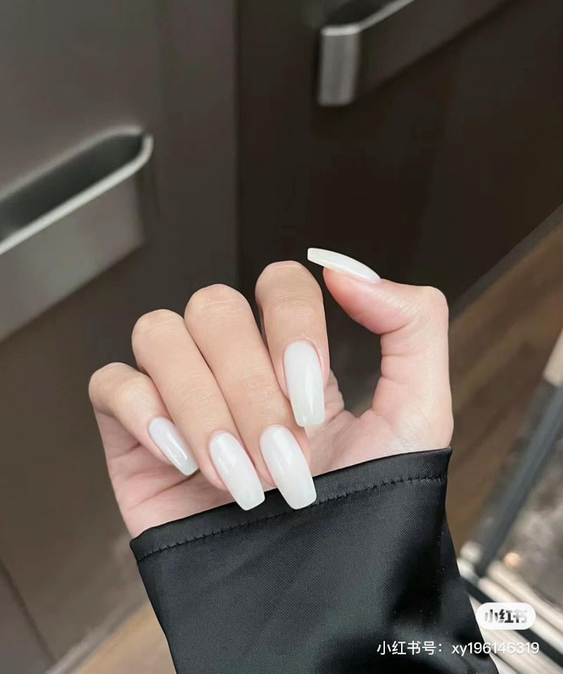 Bàn tay với móng tay dài, sơn màu trắng, trên nền áo đen.