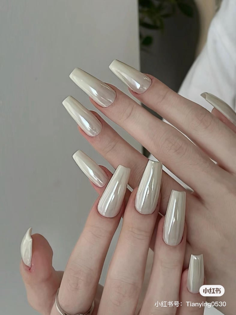 Bàn tay với móng tay dài được sơn màu ngọc trai bóng loáng, nổi bật trên nền trắng.