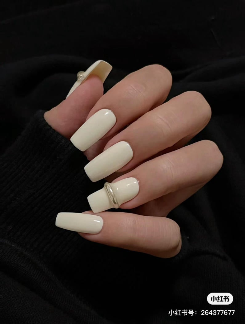 Bàn tay với móng tay dài sơn màu trắng ngà, đeo nhẫn bạc, nền áo đen.