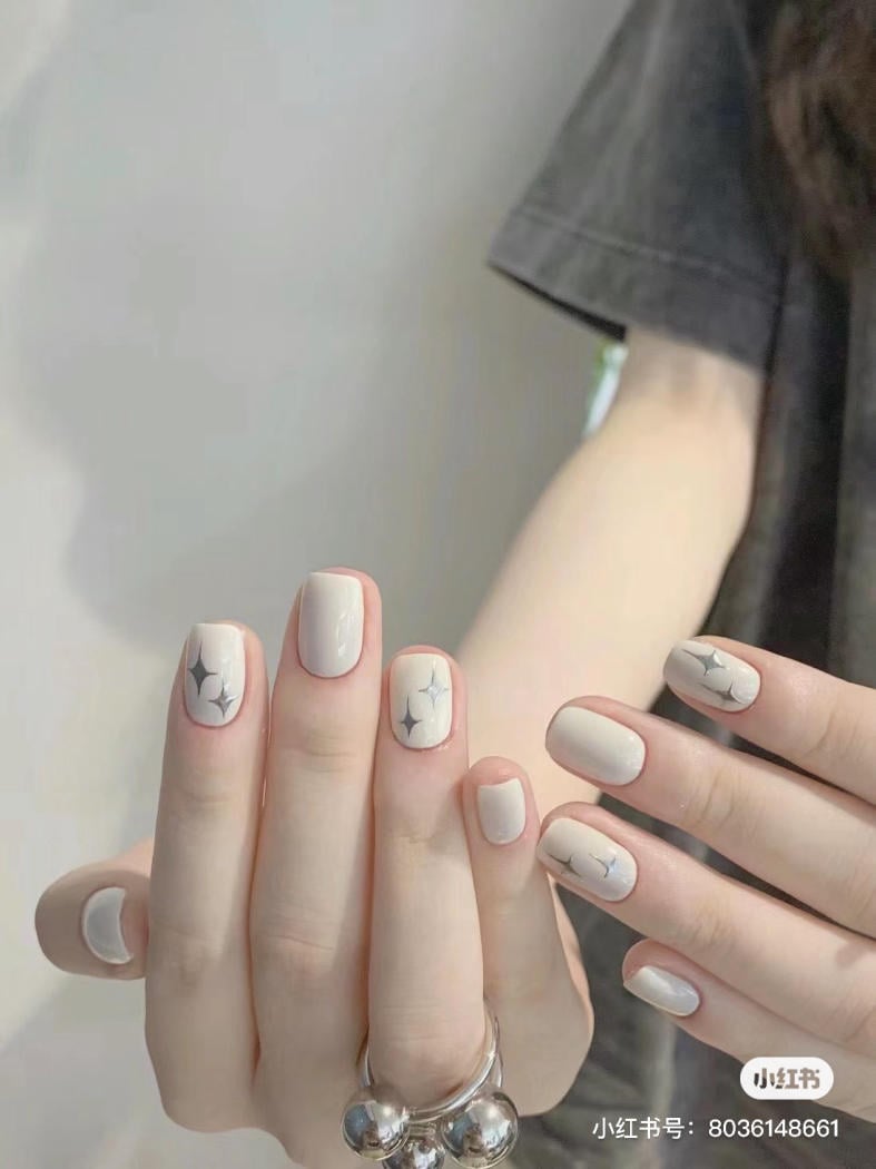 Bàn tay với móng tay sơn màu trắng, họa tiết ngôi sao, đeo nhẫn bạc, nền áo tối màu.