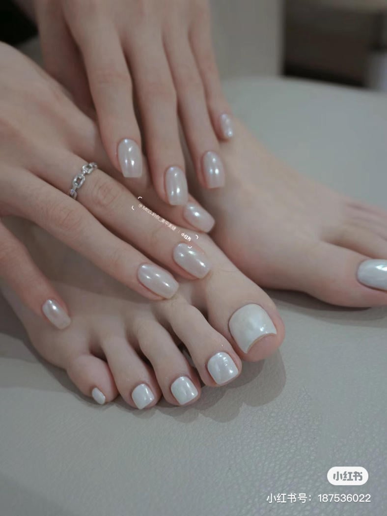 Bàn tay và chân với móng được sơn màu trắng ngọc trai, một ngón tay có đeo nhẫn bạc đơn giản.