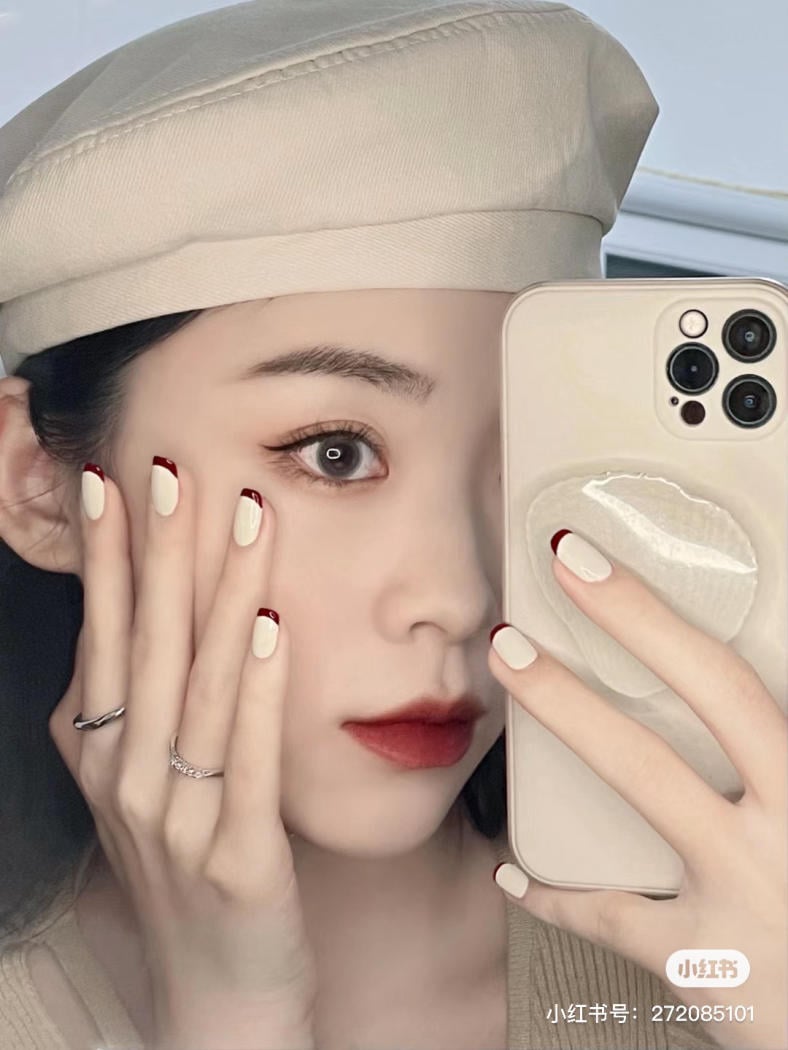 Người đội mũ beret màu be, chụp ảnh selfie bằng điện thoại, móng tay sơn màu trắng và đỏ.