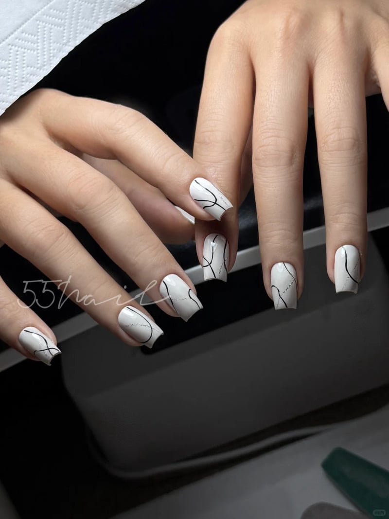Hai bàn tay với móng tay sơn màu trắng, họa tiết đường kẻ đen nghệ thuật trên nền đen.