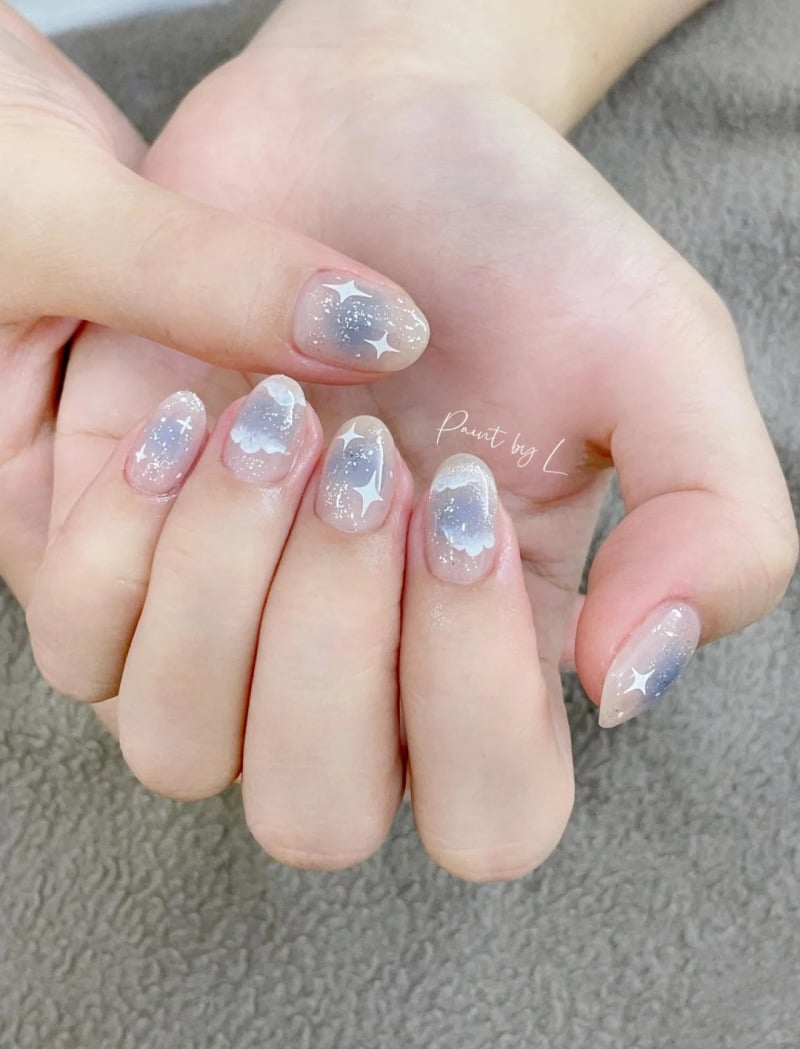 Móng tay được trang trí với họa tiết đám mây và ngôi sao, nền màu xanh nhạt và nhũ lấp lánh.
