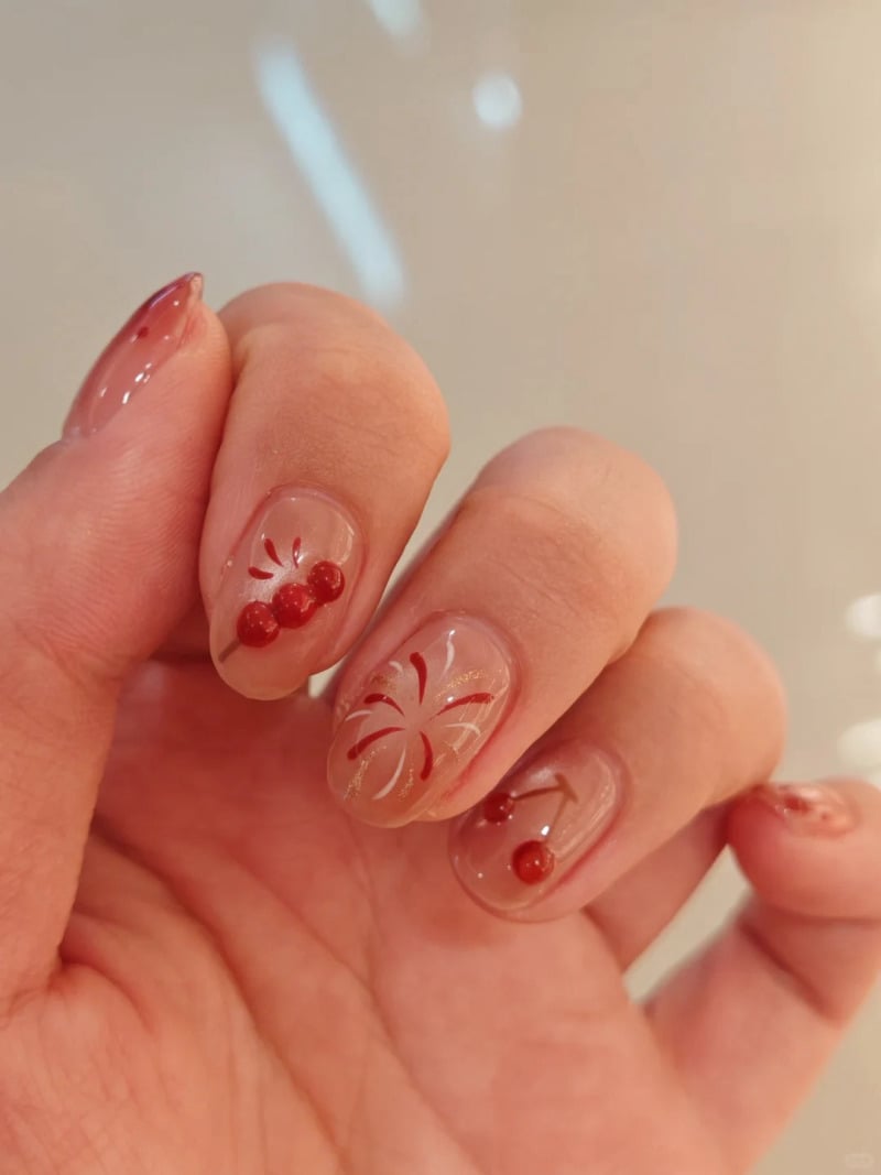 Móng tay được sơn màu trong suốt, trang trí họa tiết hoa và quả màu đỏ.