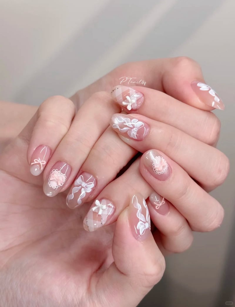 Bàn tay với móng tay được trang trí hoa văn trắng và hồng tinh tế trên nền màu nude, tạo cảm giác nhẹ nhàng và thanh lịch.