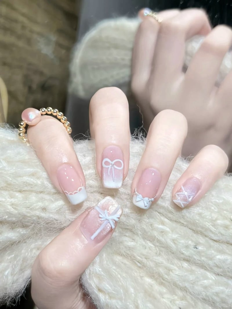 Bàn tay với móng tay sơn màu nude, trang trí họa tiết nơ trắng, cầm một vật liệu len màu sáng.
