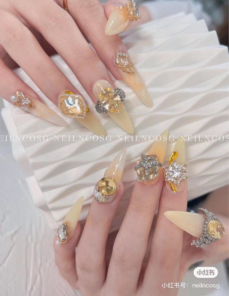 Bàn tay với móng tay dài, nhọn được trang trí bằng đá quý lấp lánh và màu sơn bóng.