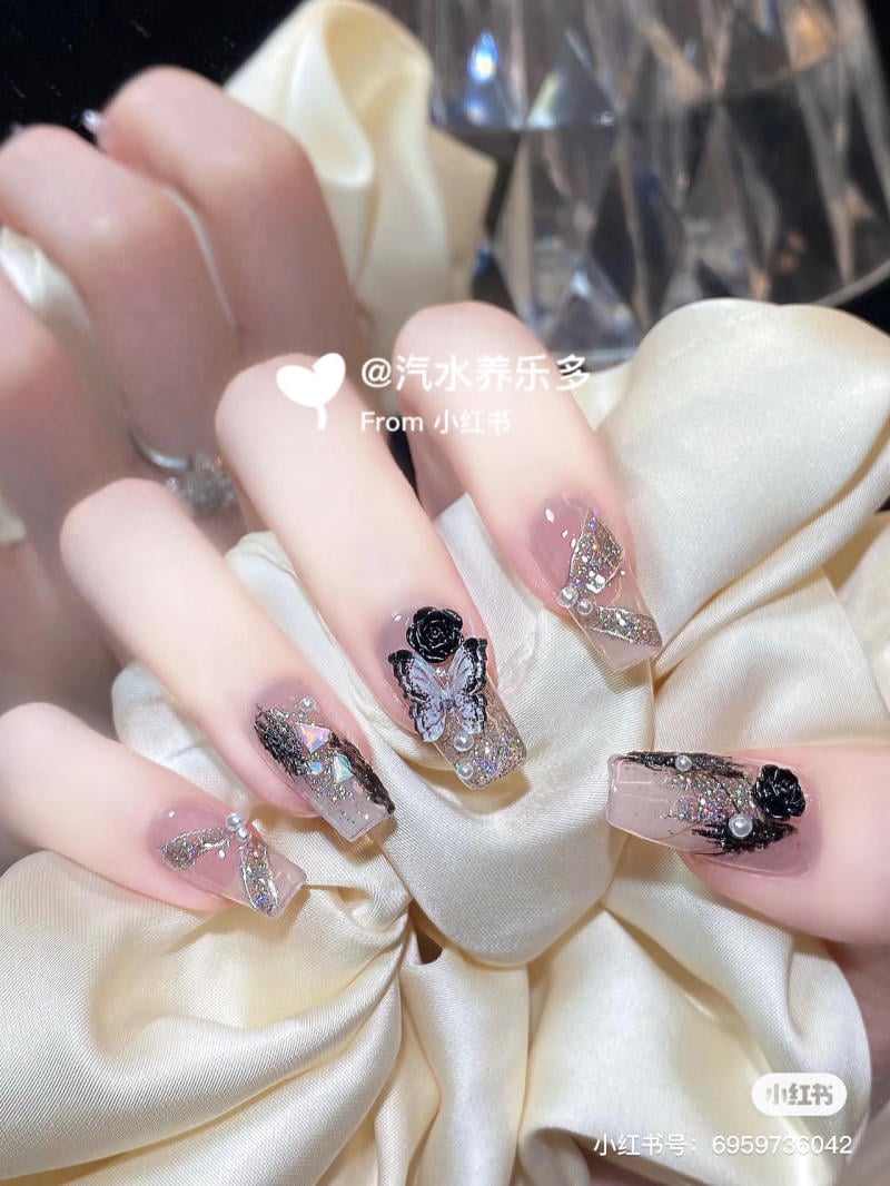 Bàn tay với móng tay được trang trí hoa văn và phụ kiện bắt mắt, nền là vải màu sáng.