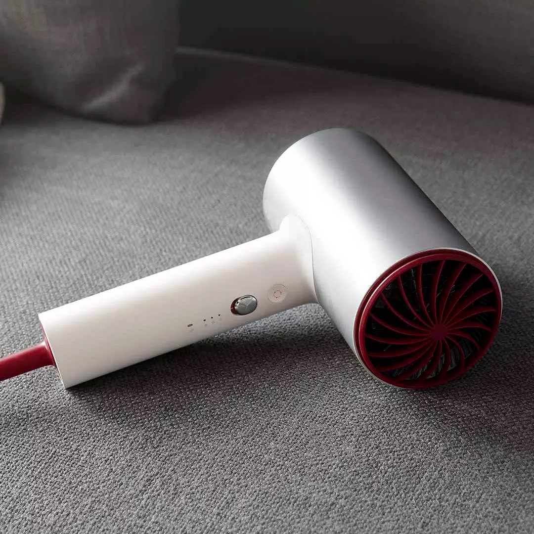 Máy sấy tóc màu trắng và đỏ đặt trên bề mặt vải xám, thiết kế hiện đại và tối giản.