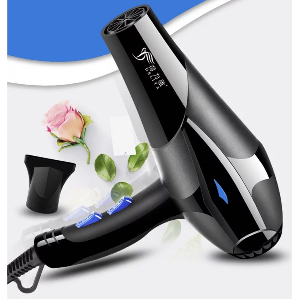 Máy sấy tóc màu đen với các nút điều khiển màu xanh dương, kèm đầu sấy và hoa hồng trang trí bên cạnh.