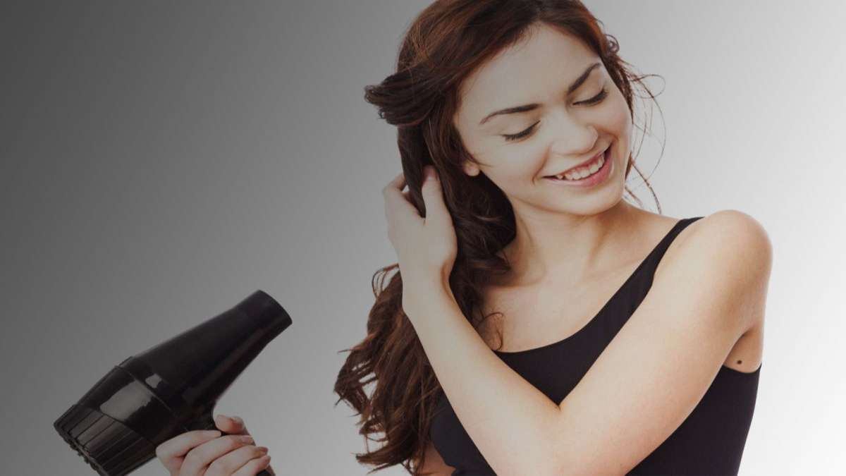 Người phụ nữ cầm máy sấy tóc, mỉm cười và chạm vào tóc, nền xám chuyển sang trắng.