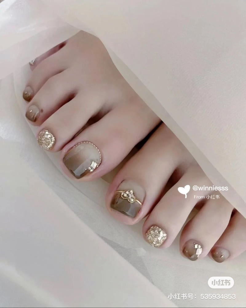 Bàn chân với móng được trang trí họa tiết và đá lấp lánh, màu sắc chủ đạo là nâu và vàng ánh kim.