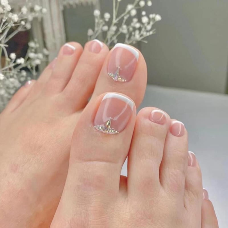 Móng chân được trang trí với sơn màu hồng nhạt và viền trắng, có đính đá lấp lánh trên ngón cái.