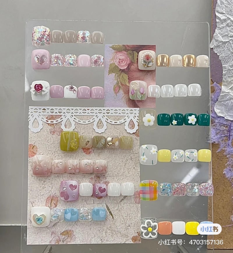 Bảng mẫu móng tay giả với nhiều màu sắc và họa tiết khác nhau được trưng bày trên nền hoa văn nhẹ nhàng.
