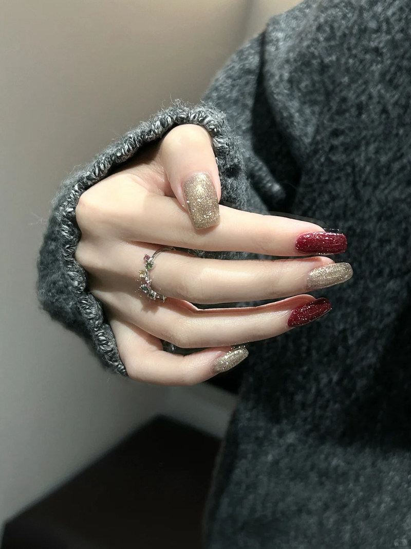 Tay đeo nhẫn, móng tay sơn lấp lánh màu vàng và đỏ, áo len xám.