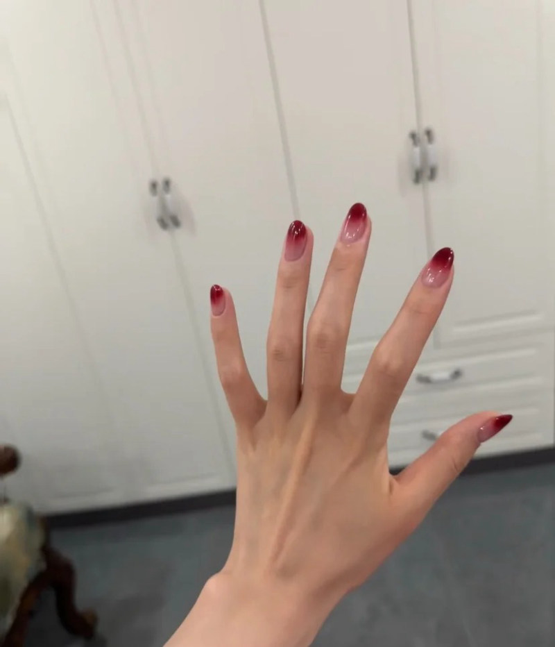 Bàn tay với móng tay được sơn màu đỏ, nền là tủ màu trắng có tay nắm kim loại.