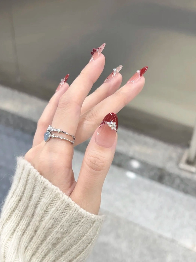 Bàn tay đeo nhẫn, móng tay dài được sơn và trang trí với họa tiết đỏ và lấp lánh, áo len màu sáng.