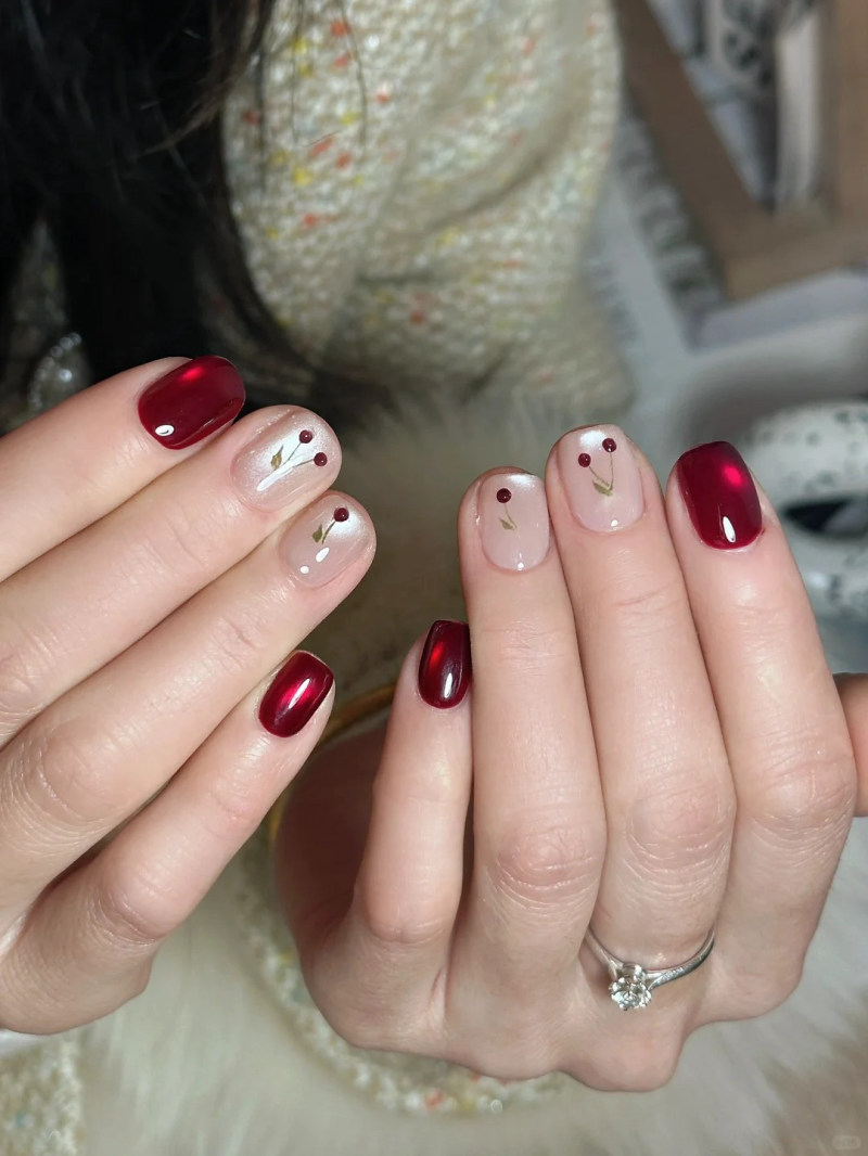 Hai bàn tay với móng tay được sơn đỏ bóng và thiết kế hoa văn nhẹ nhàng trên nền màu trắng.