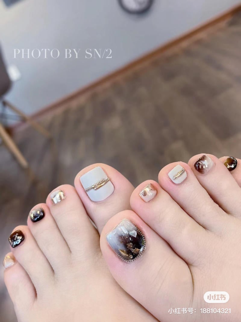 nai-chan-dinh-da__2__29057db0f5fb4a1a834d66fe4395dddc Bàn chân với móng được trang trí họa tiết đa dạng và màu sắc phong phú, trên nền sàn gỗ.