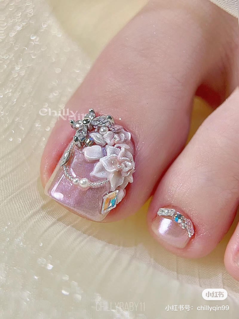 nai-chan-dinh-da__7__4784e2e834dd47f58fe215d4ff4eb3b8 Móng chân được trang trí với hoa nổi, đá quý và hạt ngọc, nền màu hồng ánh kim.