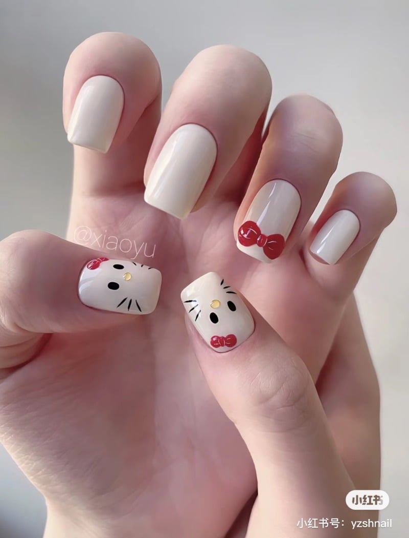 Bàn tay với móng tay sơn màu trắng, trang trí hình mèo và nơ đỏ.