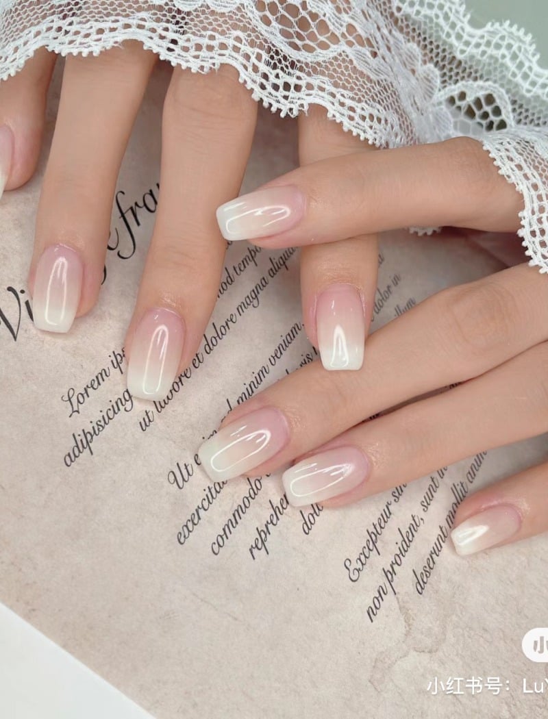 Bàn tay với móng tay sơn màu trắng sữa, đặt trên nền giấy có chữ, phủ nhẹ lớp ren trắng.
