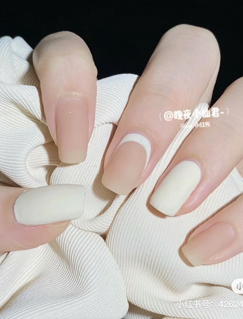 Bàn tay với móng tay được sơn màu trắng và be, cầm một mảnh vải màu trắng.