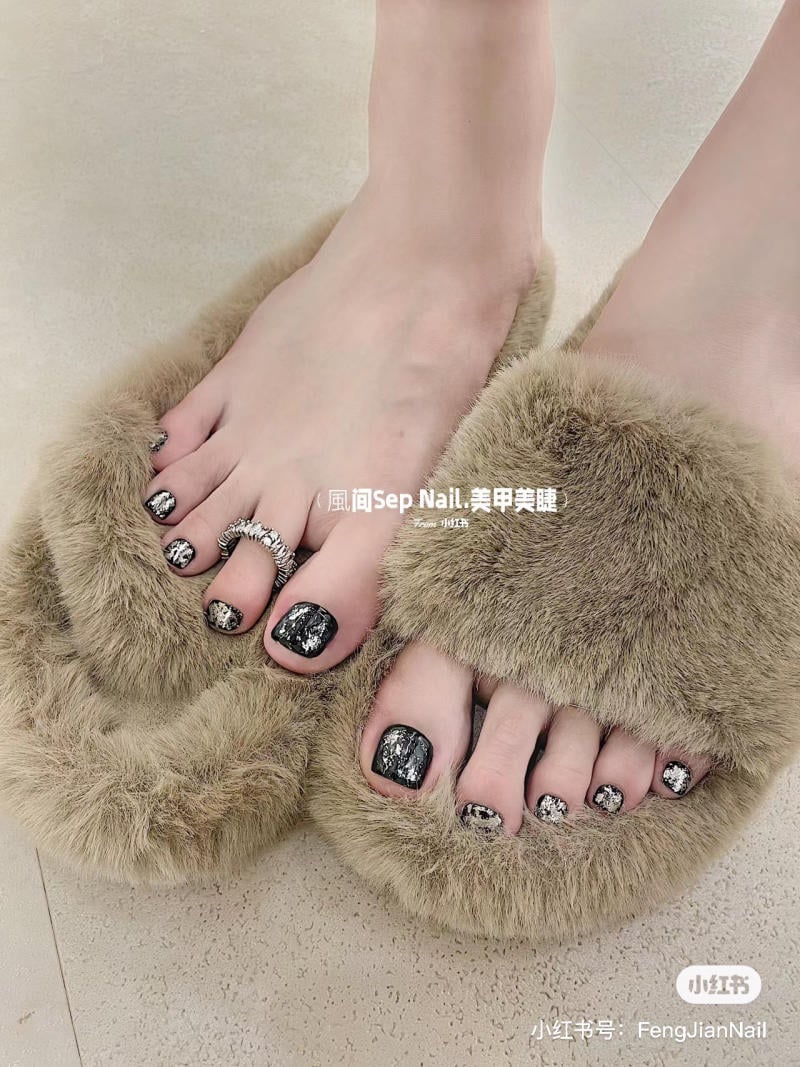 nail-chan-dinh-da__11__a71eb7fa208d448c846b8a488f6146bc Đôi chân với móng chân sơn họa tiết đen bạc, đi dép lông mềm mại màu nâu nhạt trên nền gạch sáng.